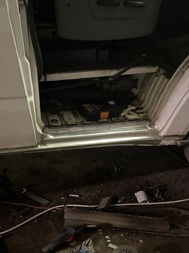 Open vehicle door showing tools and parts inside and on the ground.