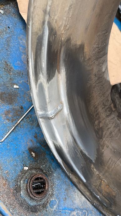 Close-up of a worn and repaired metal rim on a blue surface.