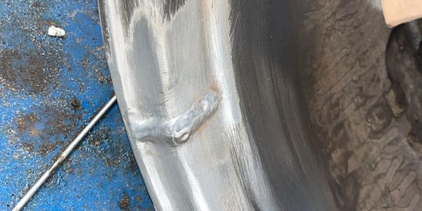 Close-up of a worn and repaired metal rim on a blue surface.
