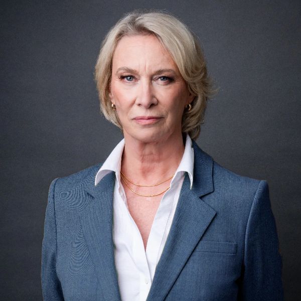 Confident mature woman in professional attire against a dark background.