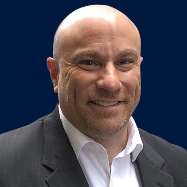 Smiling bald man in a suit against a dark blue background.