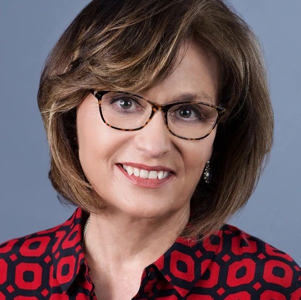 Smiling woman with glasses and a red patterned shirt against a gray background.