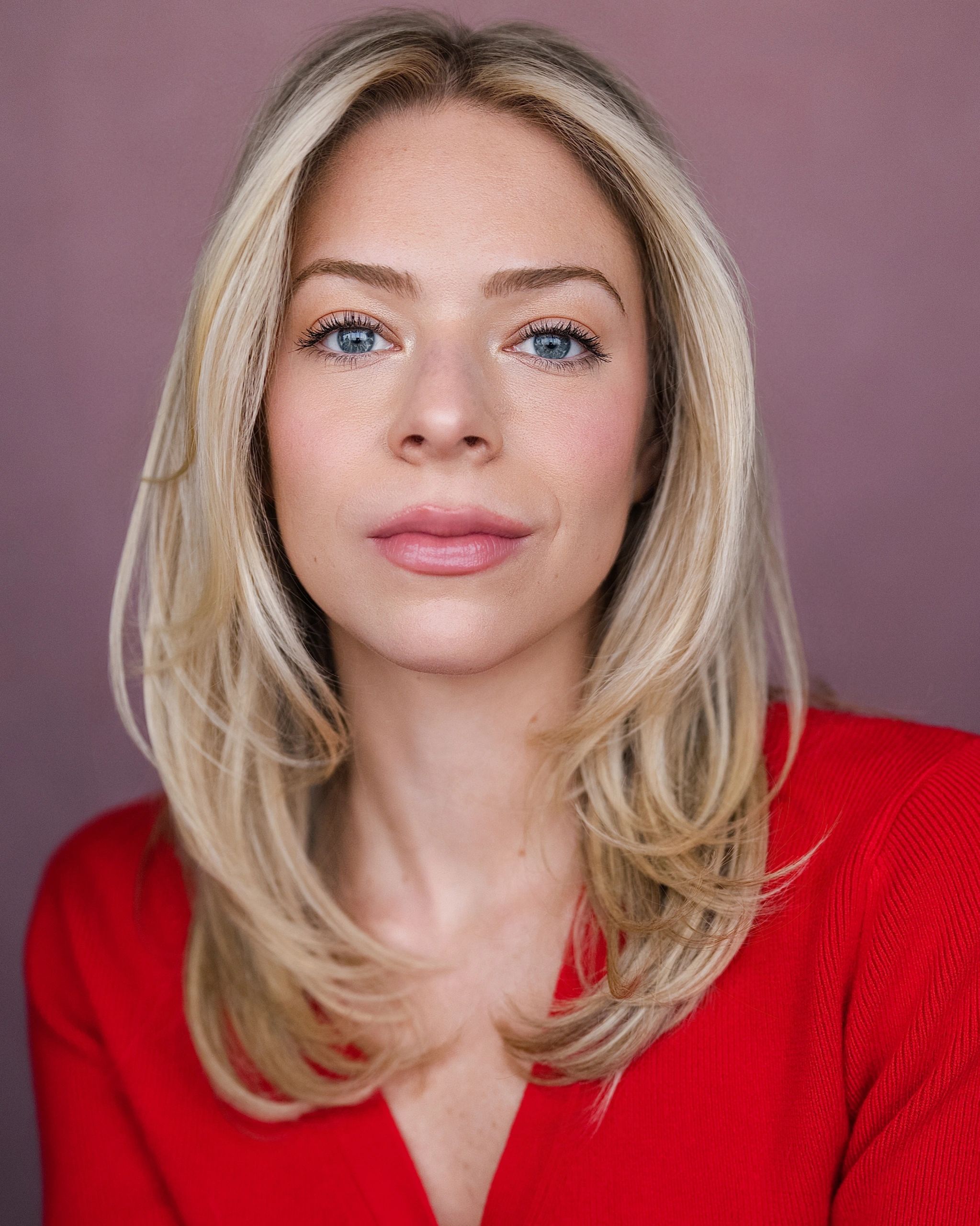 Close-up portrait of a blonde woman with blue eyes and a red top.