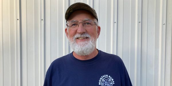 Smiling elderly man with a white beard wearing glasses and a cap.