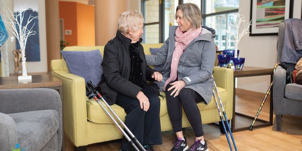 Young white woman sitting on sofa facing senior white woman, chatting, poles resting on sofa 