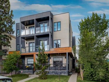 Modern three-story residential building with balconies and greenery.