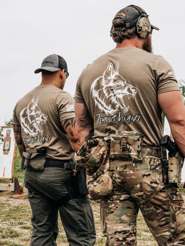 Two men in tactical gear with 'Tempus Verandi' wolf logo shirts at a shooting range.