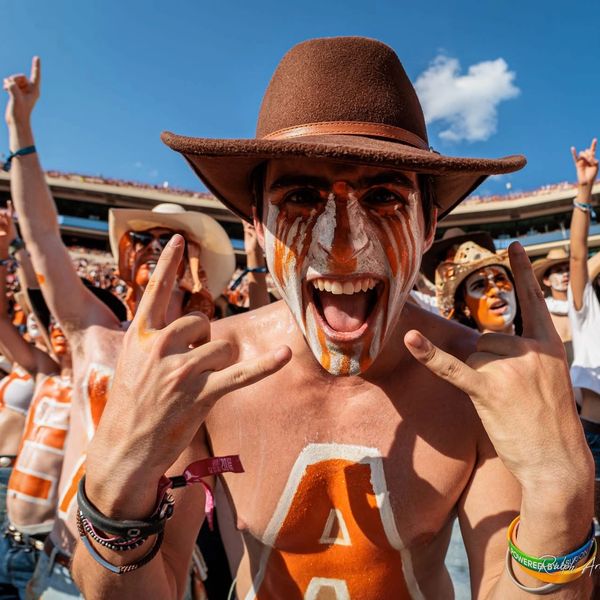 Excited sports fan with face paint and cowboy hat at stadium.