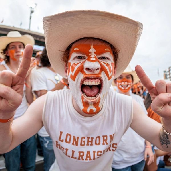 Excited fan with face paint and cowboy hat cheers for Longhorn Hellraisers.