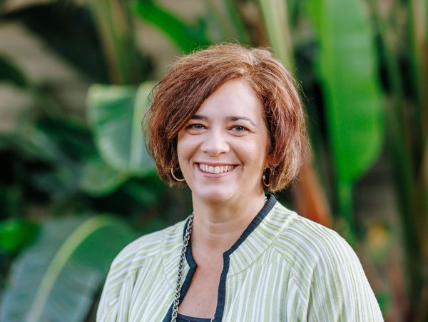 Smiling woman outdoors with green foliage background.