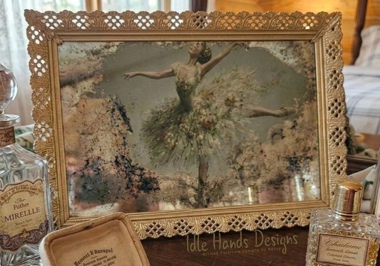 Vintage framed ballerina artwork with ornate lace border on a wooden table.