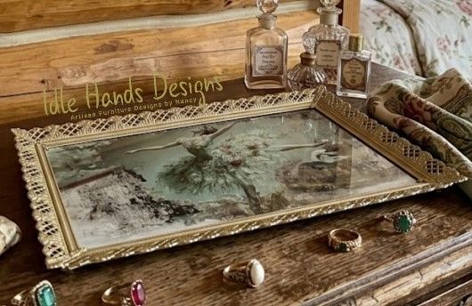 Antique mirrored tray with ornate edges on a wooden surface, surrounded by vintage rings and perfume bottles.