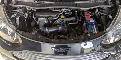 Open hood revealing a clean Aston Martin engine bay with visible battery and fluid reservoirs.