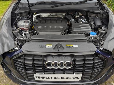 Open hood of an Audi car showing the engine and front grille with a custom license plate.