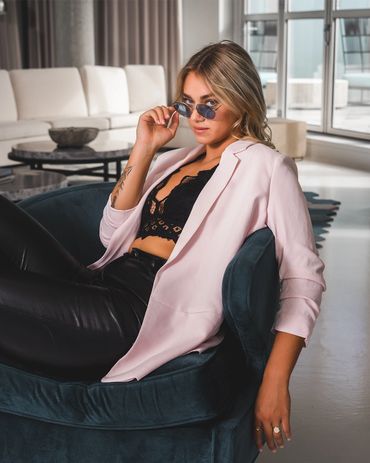 Fashion photography of a confident woman in chic outfit posing indoors with stylish sunglasses.