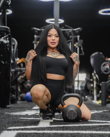 girl with neck tattoo posing with a kettlebell on black turf in a dark gym