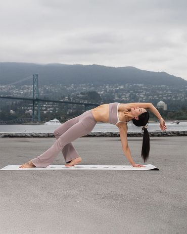 athletic fitness girl performing yoga pose in on seawall boardwalk in front of mountains and ocean