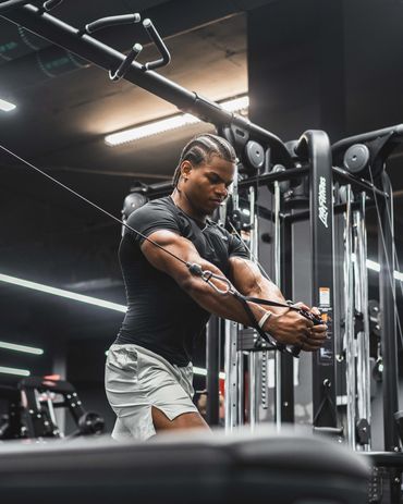 fitness photography of a fit man with braids in his hair performing cable chest fly in a gym