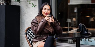 girl wearing stylish outfit with a nice coat sips coffee while sitting at a table