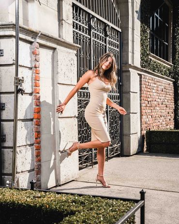 Fashion photography of a woman in a beige dress posing elegantly in bright outdoor lighting.