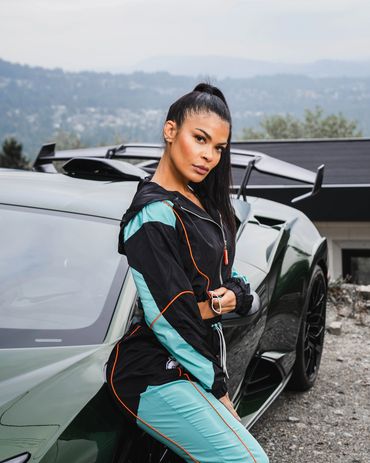 Fashion photography of a woman in sporty outfit posing confidently beside a lamborghini.