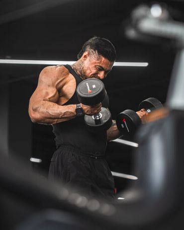 fitness photography of a jacked man curling dumbbells in a dark gym