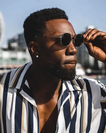 Fashion portrait of a stylish man in striped shirt and sunglasses under bright sunlight.