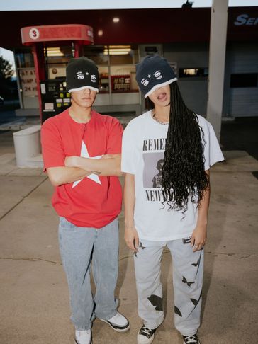 Two young people wearing graphic beanies covering their eyes at a gas station.