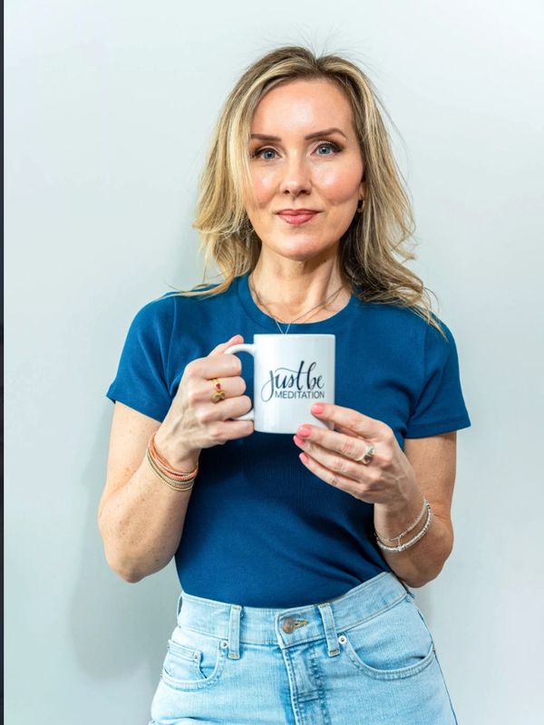 Woman holding a mug with "Just Be Meditation" text.