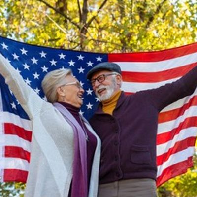 Happy elderly couple holding American flag outdoors in autumn.