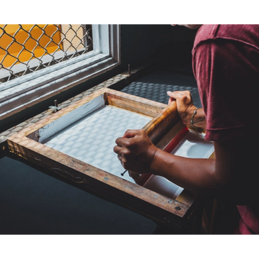Person using a wooden frame and roller for screen printing near a window.