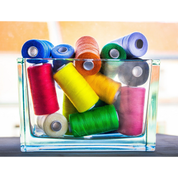 A glass container filled with colorful sewing thread spools.