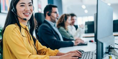 Smiling customer service agent wearing a headset typing at her computer.