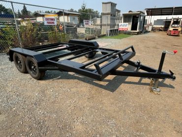 Black flatbed trailer on gravel ground outside.