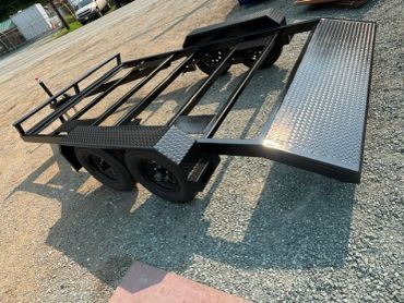 Black metal trailer on gravel surface.