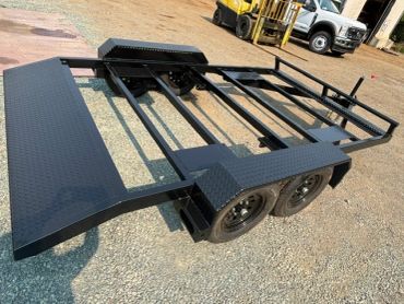 Black metal trailer frame with wheels on gravel.