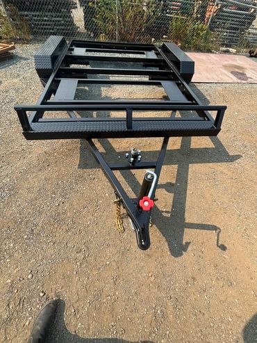 Black utility trailer frame on dirt ground.