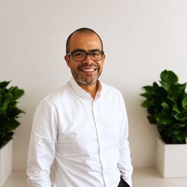 Smiling man in glasses and white shirt standing indoors with plants.