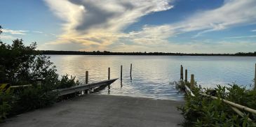 Sunset over a peaceful lake with docks and plants.
