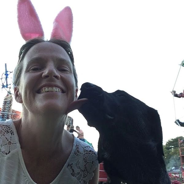 Mrs H, wearing rabbit ears, is being licked on the cheek by a black dog at the fair