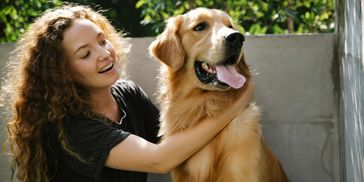 A woman joyfully pets a happy golden retriever outdoors.