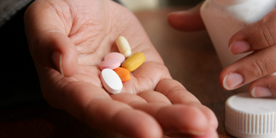 Hand holding various colorful pills with a medicine bottle nearby.
