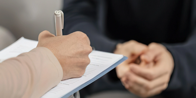 Person signing a document while another waits with hands clasped.