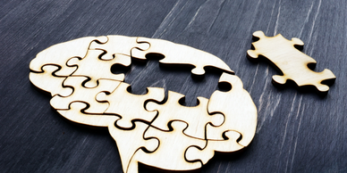 Wooden brain puzzle with one missing piece next to it on a dark surface.