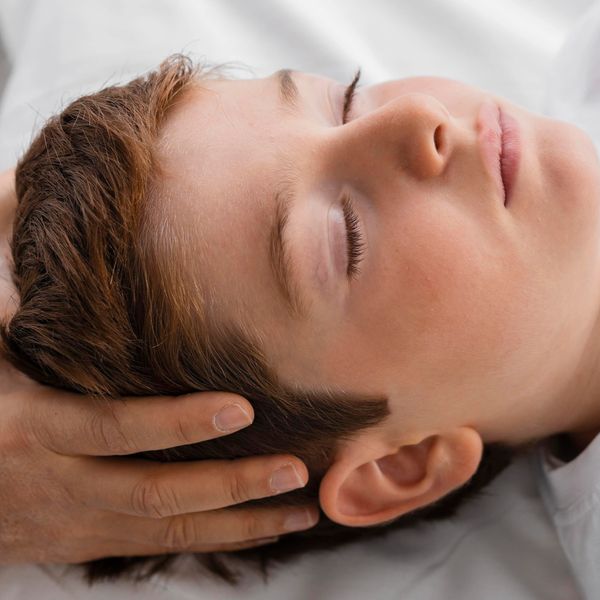 Boy's face is calm and serene. His eyes are closed. Hands gently hold acupressure points on the side