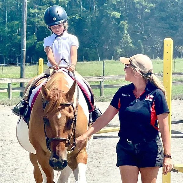 A young girl rides a horse while a woman guides them outdoors.