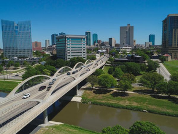 A modern arched bridge over a river in an urban cityscape.