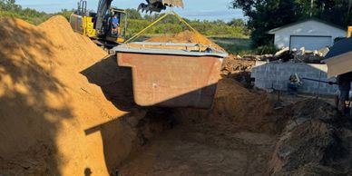 Excavator lifting a large metal container filled with sand at a construction site.