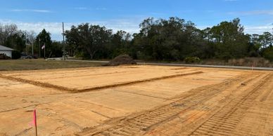 A cleared and leveled construction site with marked areas and trees in the background.