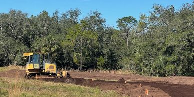 Bulldozer grading land near a forested area under clear sky.